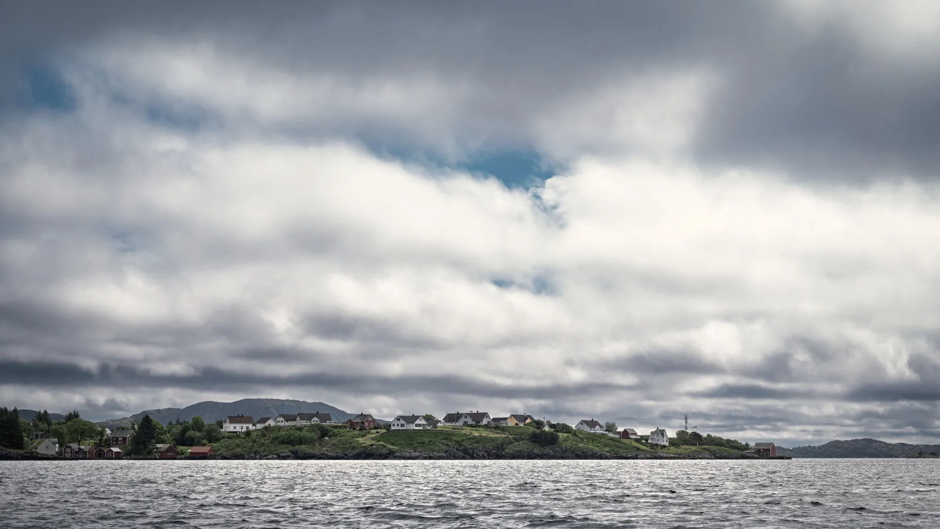 Bebyggelsen på Byrknesøy sett fra sjøen under en skyfull himmel