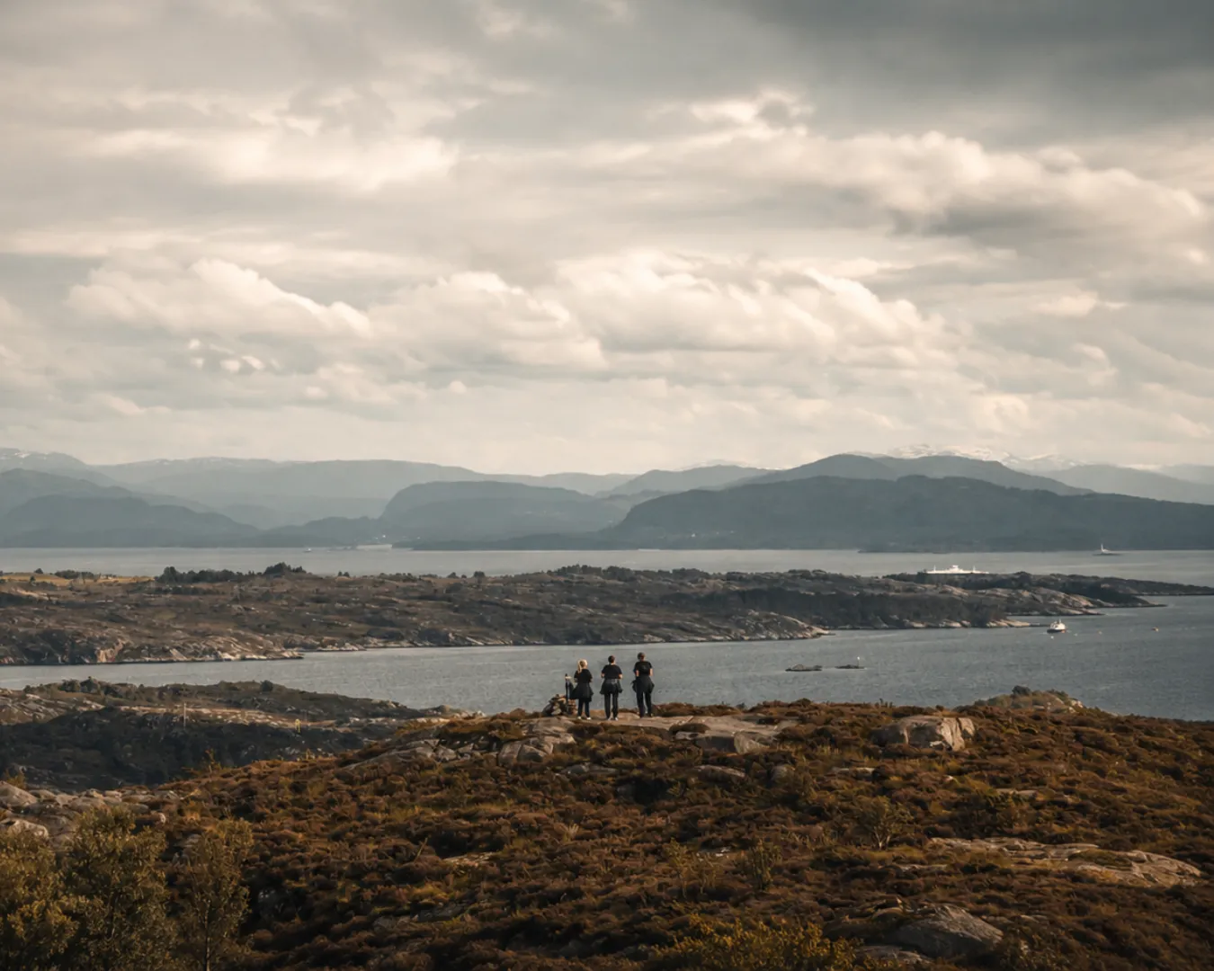 Tre personer står på en lyngkledd knaus og ser utover øyene og fjellene ved Byrknesøy