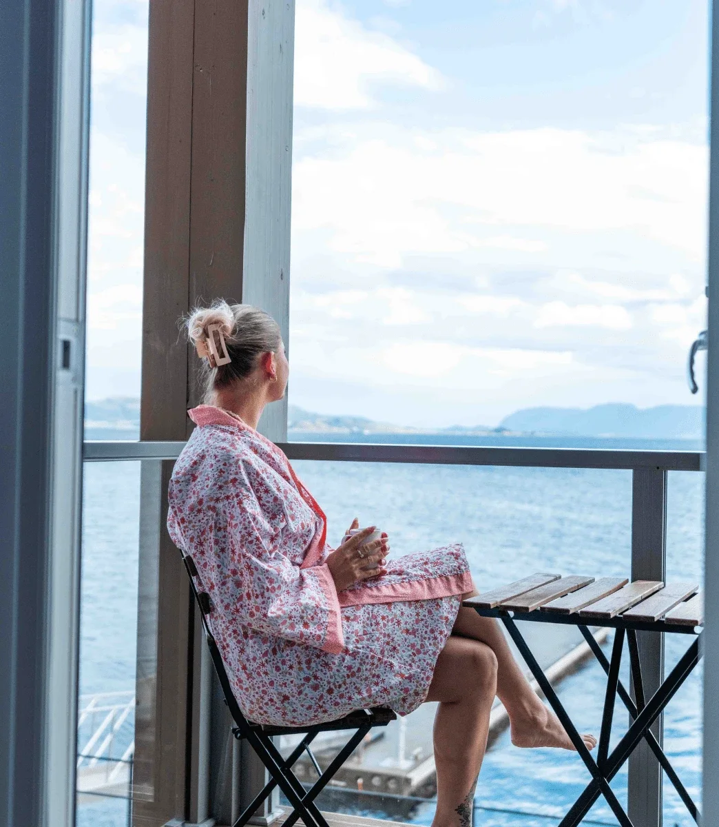 Gjest i kimono med kaffekopp på balkongen med utsikt over sjøen